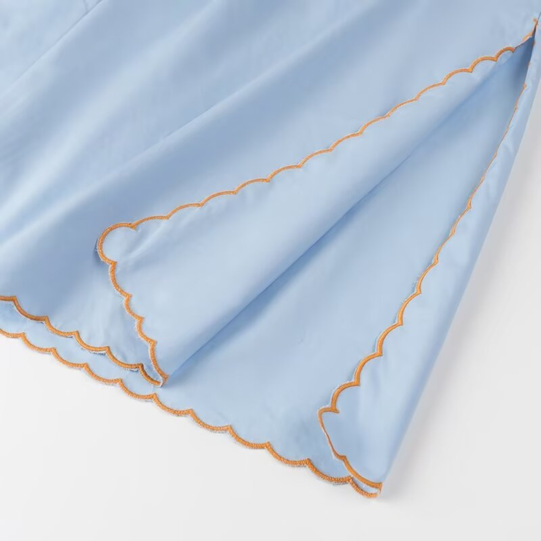 Detail des Saumrands am Danyy Zweiteiler – gewellte Kante mit orangefarbener Stickerei für feine, verspielte Sommerästhetik.