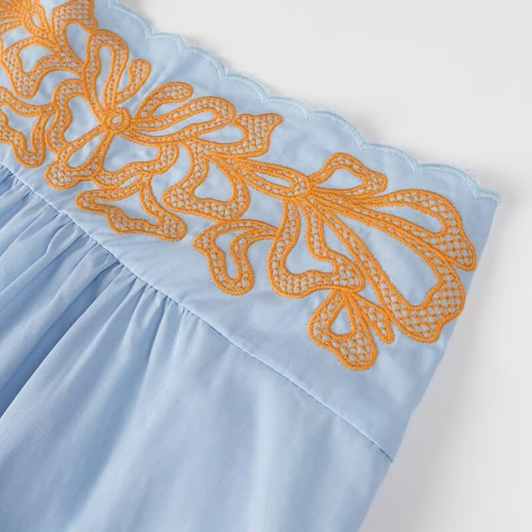 Detailaufnahme der floralen Stickerei des Danyy Zweiteilers – orangefarbene Akzente auf hellblauem Stoff für sommerliche Eleganz.