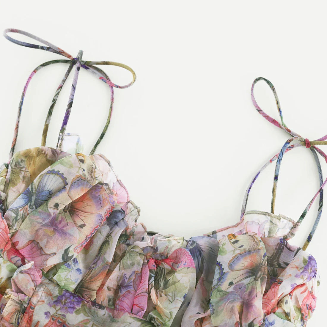 Das Karyy Florale Minikleid zeigt zarte Rüschenlagen, verspielte Träger und ein luftiges Design mit buntem floralen Schmetterlingsmuster.