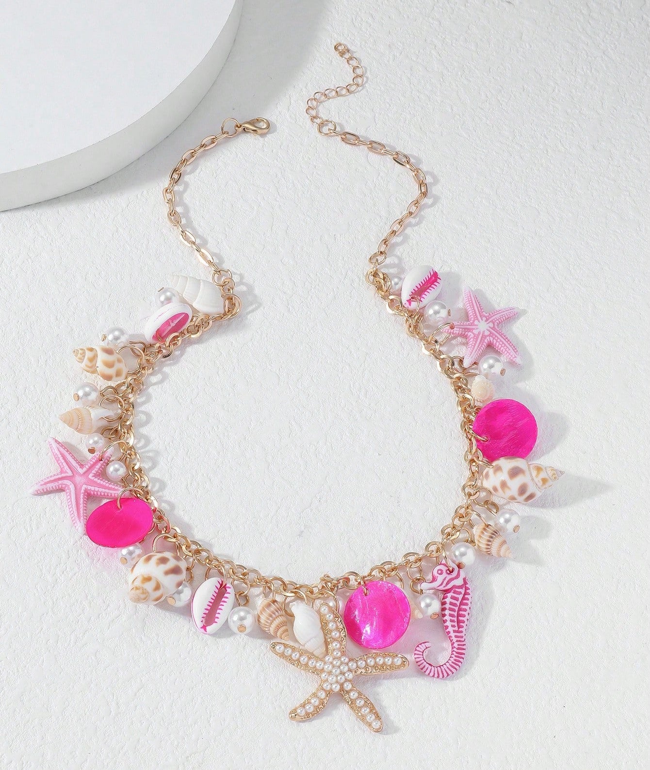Detailaufnahme der pinkfarbenen Tyfyy Seestern Muschel Halskette mit goldener Kette, Perlen, Muscheln und Seepferdchen – sommerlicher Strandlook.