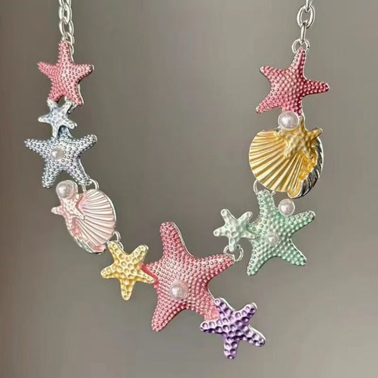 Die Maddyy Maritime Halskette von CozyWoolCraft zeigt Seesterne, Muscheln und Perlen in sanften Pastellfarben – ein verspielter Sommer-Schmuck für feminine Looks.